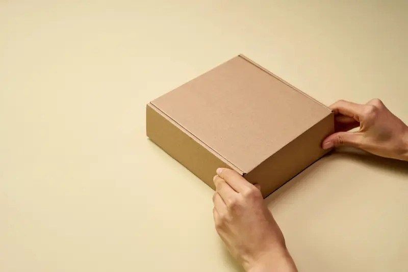 Manos cerrando una caja de cartón con un pedido listo para entregar