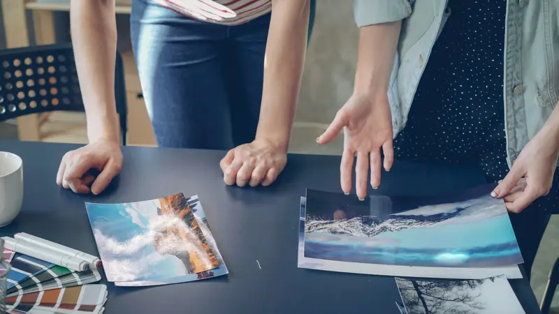 Personas revisando diseños impresos sobre una mesa, junto a una guía de colores