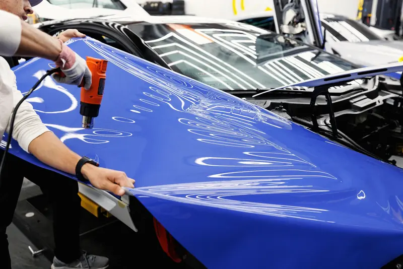 Instalador aplicando vinil adhesivo azul sobre el capó de un auto con pistola de calor